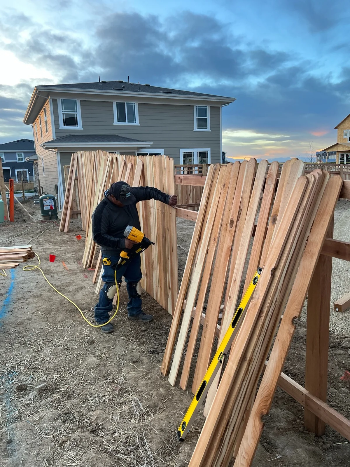 Golden Stain crew member fastening fence pickets at dusk