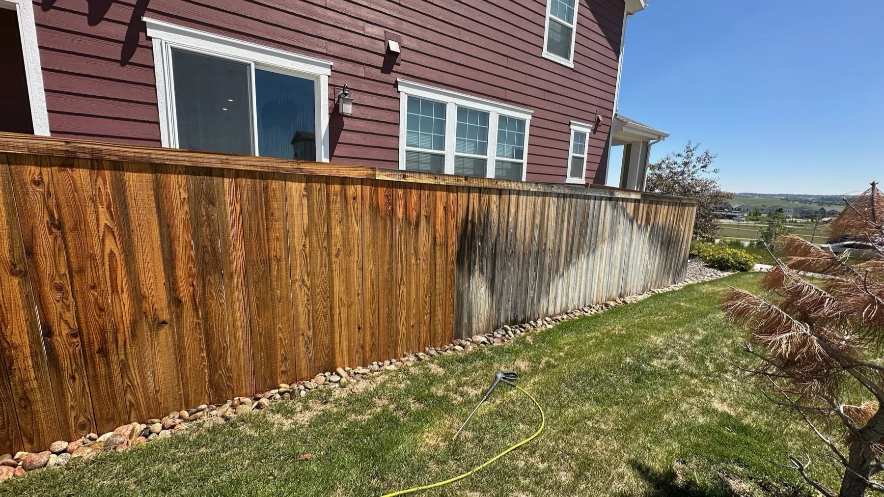 A wood fence half cleaned, showing the contrast between weathered gray and restored boards