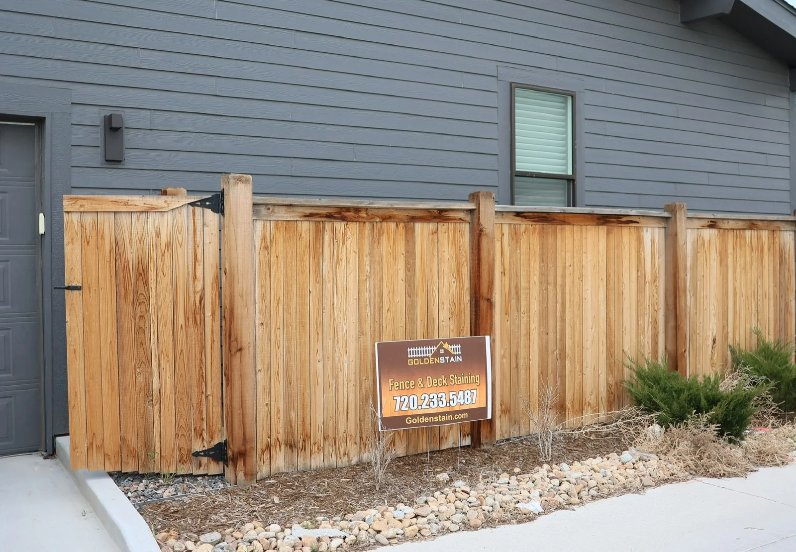 Neat stained cedar fence along a sidewalk with a Golden Stain yard sign
