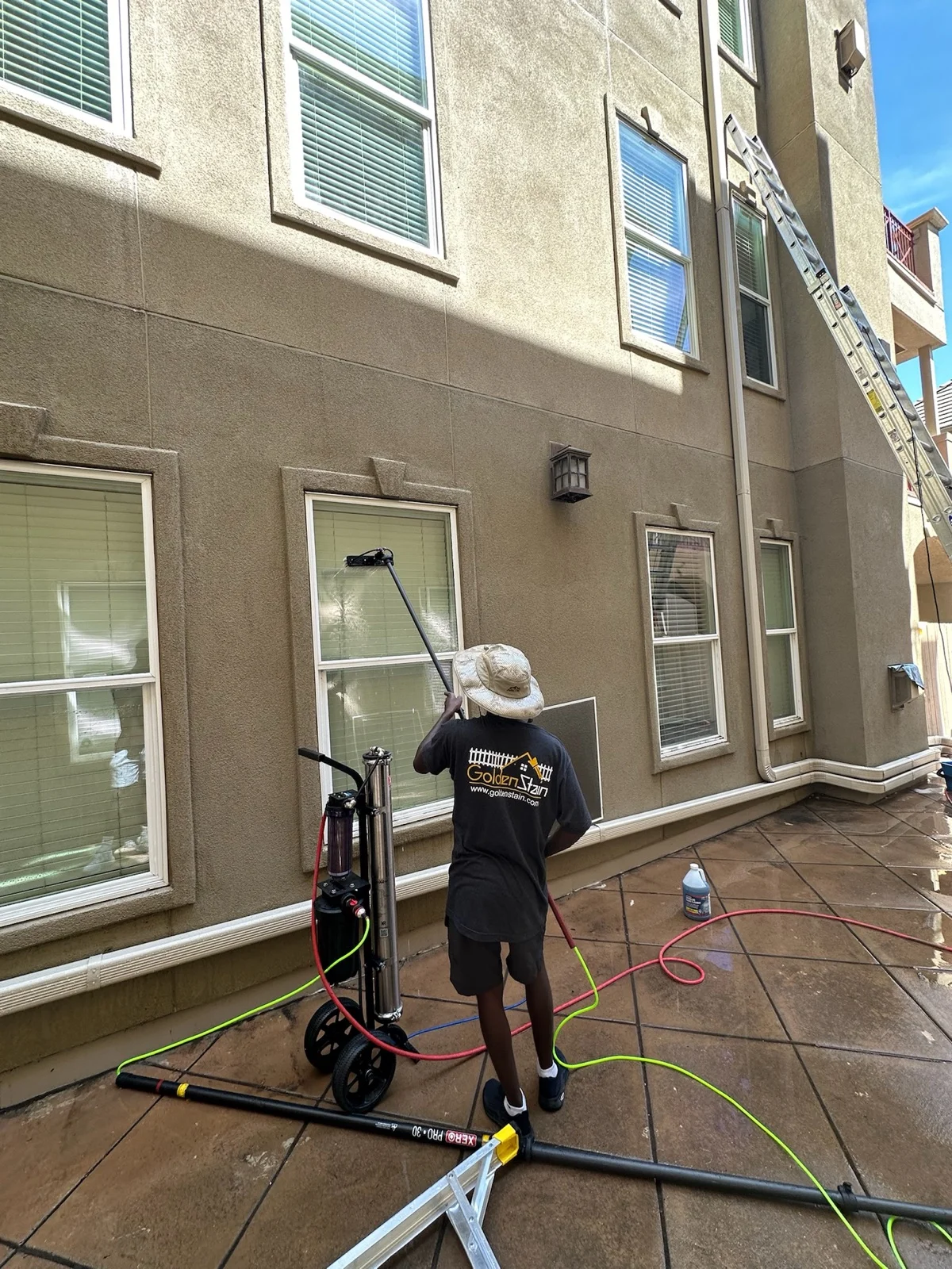 Golden Stain crew member cleaning windows with a water fed pole on a two story home